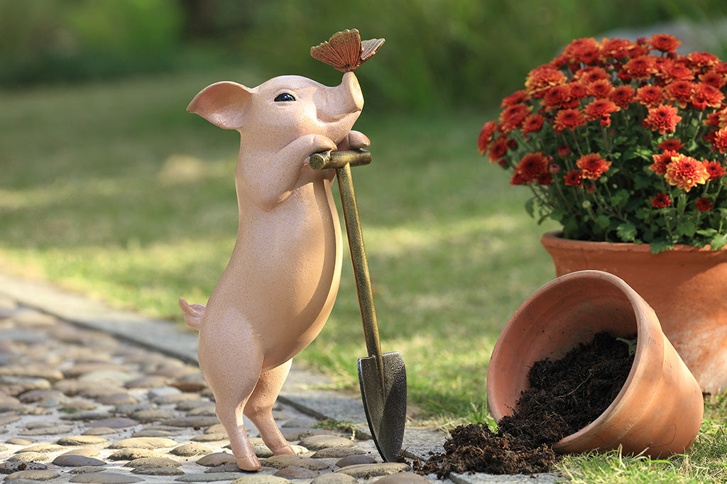A sculpture of a pig holding a shovel with a butterfly landing on it's nose.