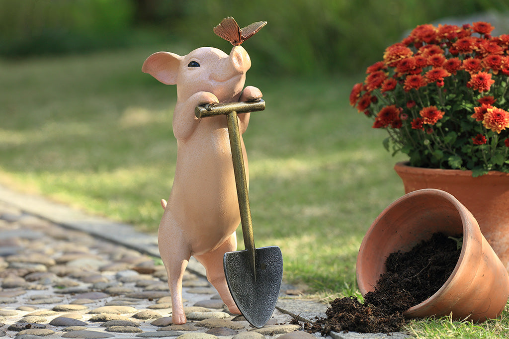 A sculpture of a pig holding a shovel with a butterfly landing on it's nose.