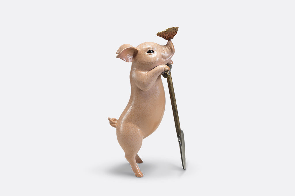 A sculpture of a pig holding a shovel with a butterfly landing on it's nose.