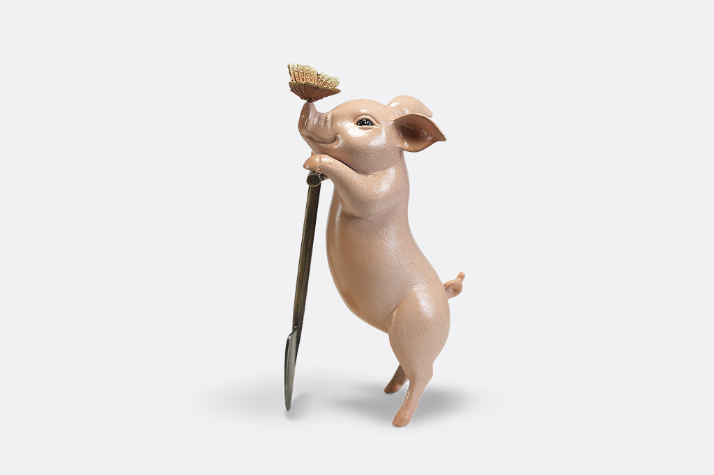 A sculpture of a pig holding a shovel with a butterfly landing on it's nose.