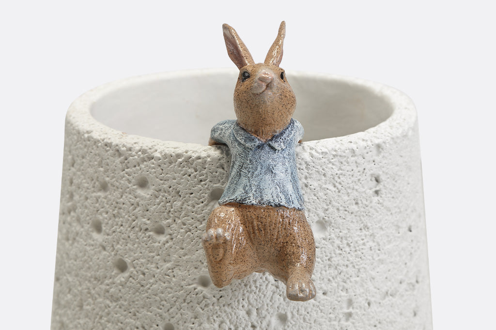 A hanging sculpture of two bunnies wearing blue shirts that dangle off of plant pots.