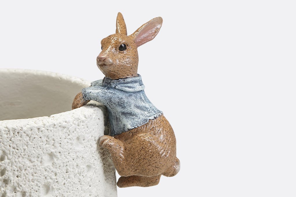 A hanging sculpture of two bunnies wearing blue shirts that dangle off of plant pots.