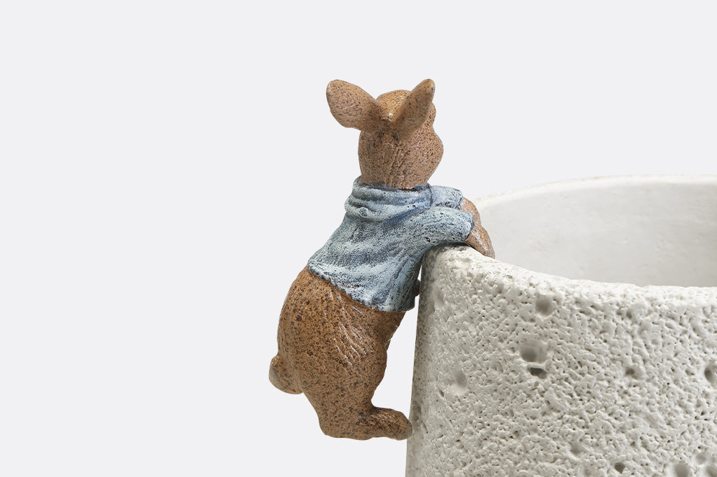 A hanging sculpture of two bunnies wearing blue shirts that dangle off of plant pots.
