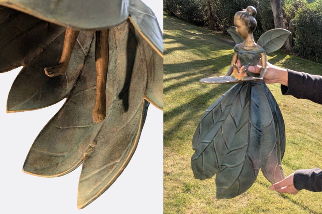 Close-up of a decorative fairy figure with leaf-like wings held by a person outdoors.