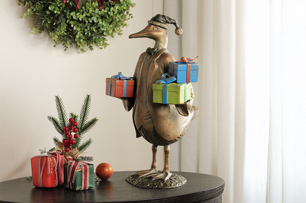 Decorative statue of a duck with gift boxes on a table, with a wreath and plants in the background.