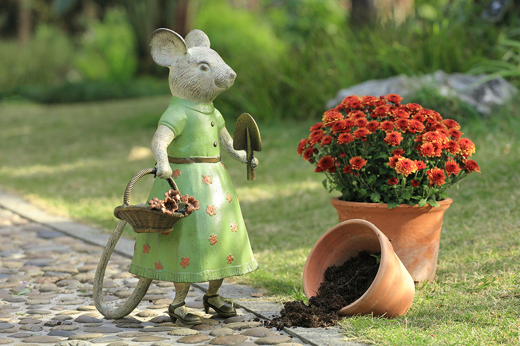A mouse in a green dress holding a shovel and a basket of flowers.