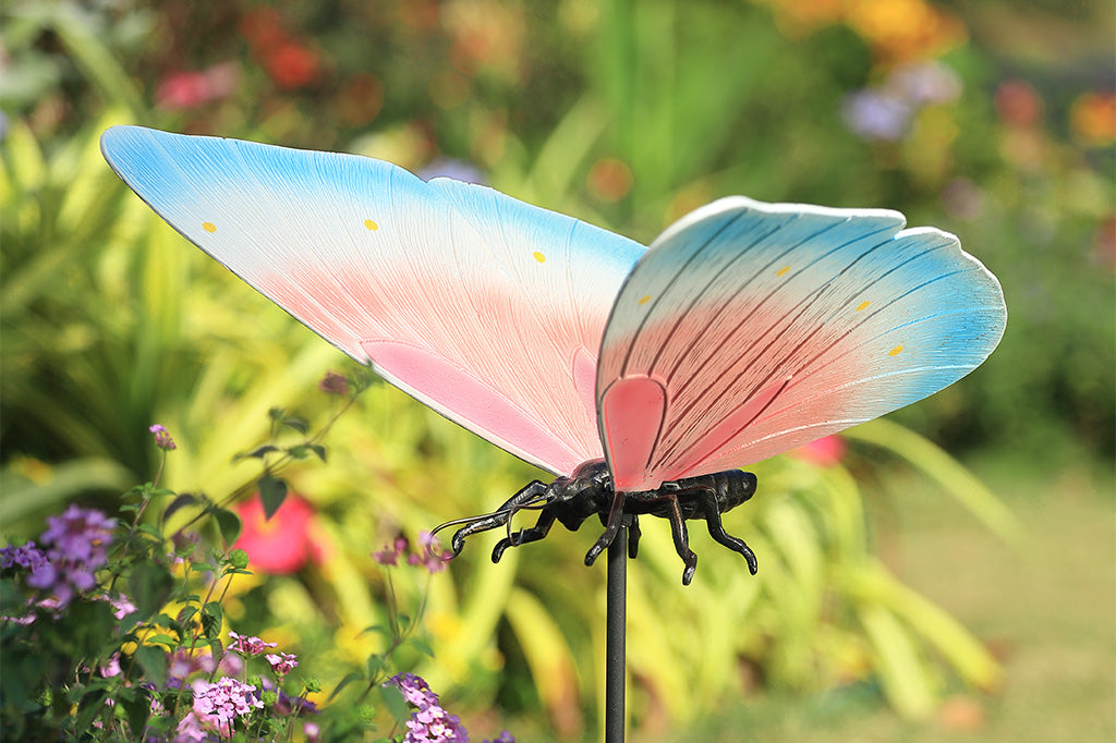 A garden stake sculpture of a butterfly with hues of light blue, white, and pink with yellow details.