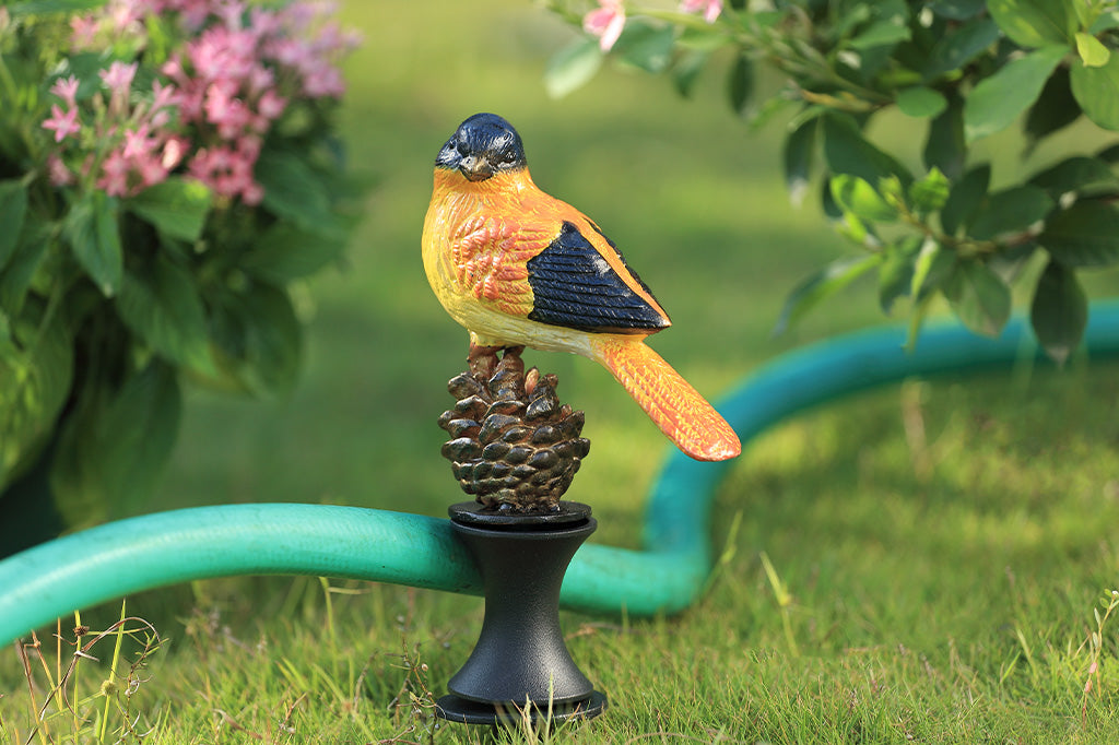 Decorative bird on a pinecone with a green hose in a garden setting