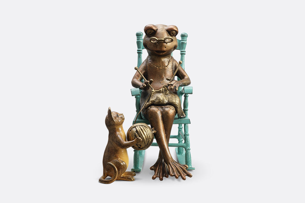Sculpture of a frog knitting on a chair with a Cat and yarn ball on a white background