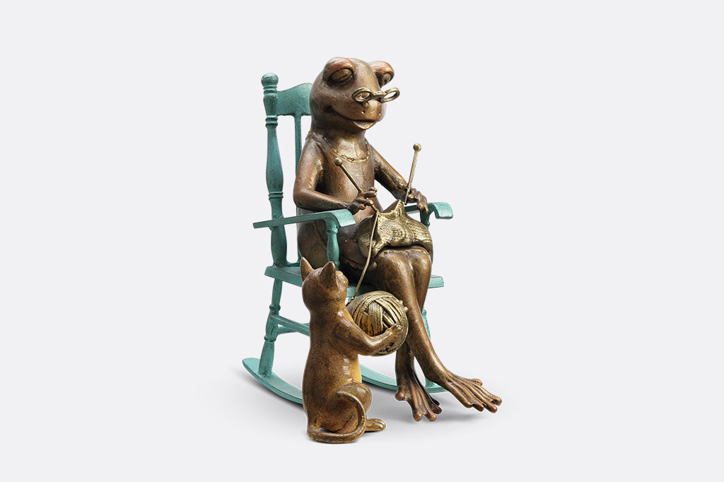 Sculpture of a frog knitting on a chair with a Cat and yarn ball on a white background