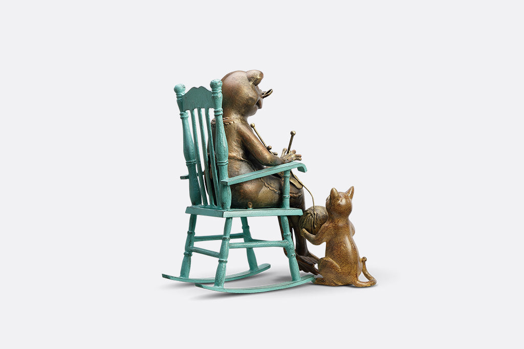 Sculpture of a frog knitting on a chair with a Cat and yarn ball on a white background