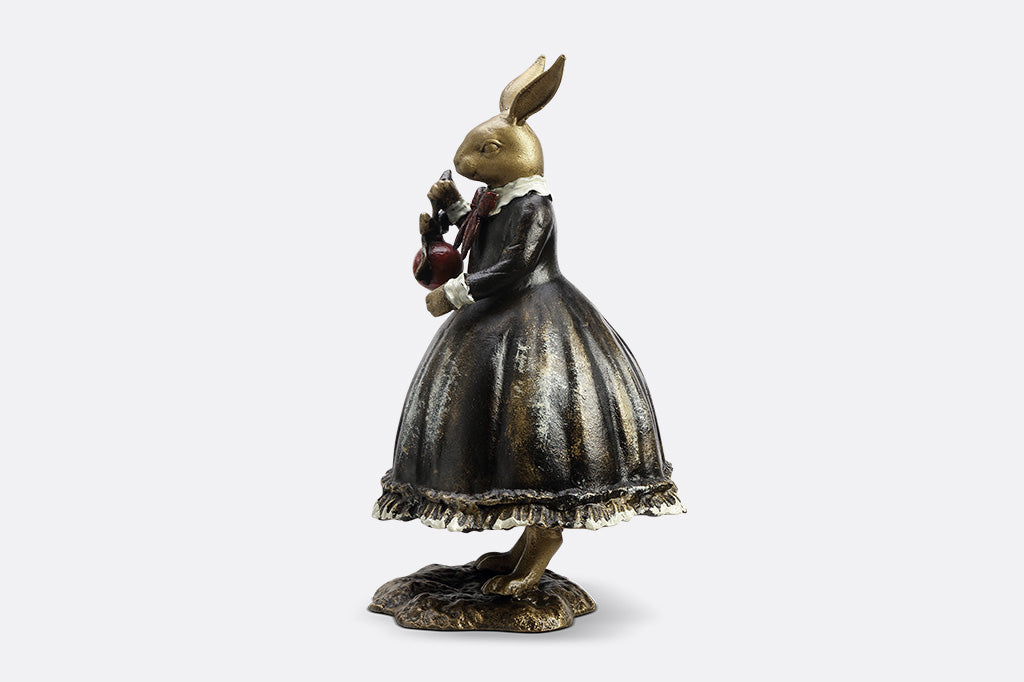 Sculpture of a bunny dressed in Victorian Era attire holding a red Chirstmas ornament.