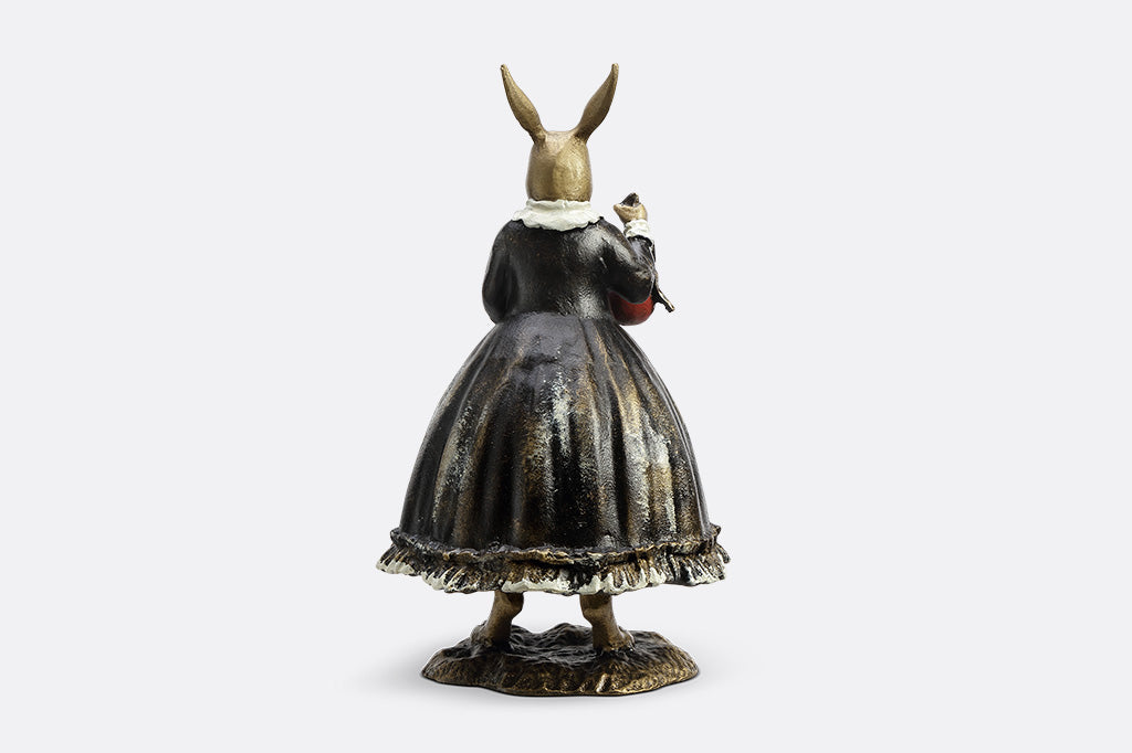 Sculpture of a bunny dressed in Victorian Era attire holding a red Chirstmas ornament.