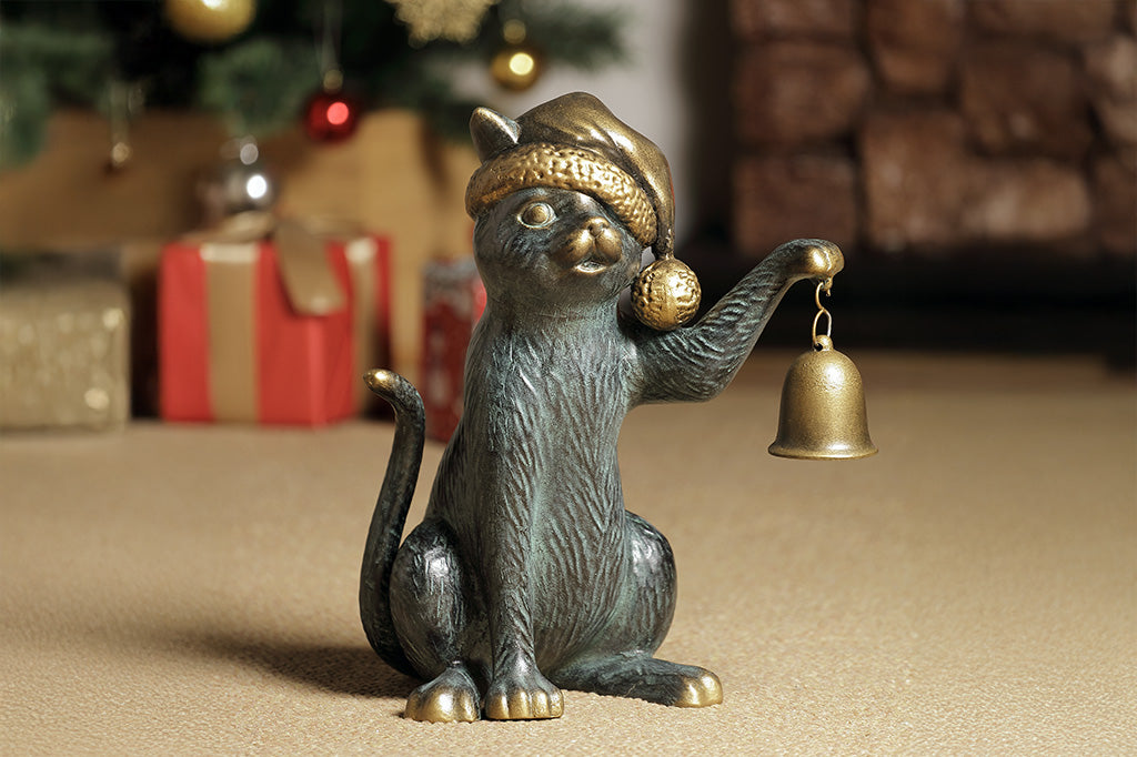 Cat figurine with a bell in a festive setting with Christmas decorations and presents.