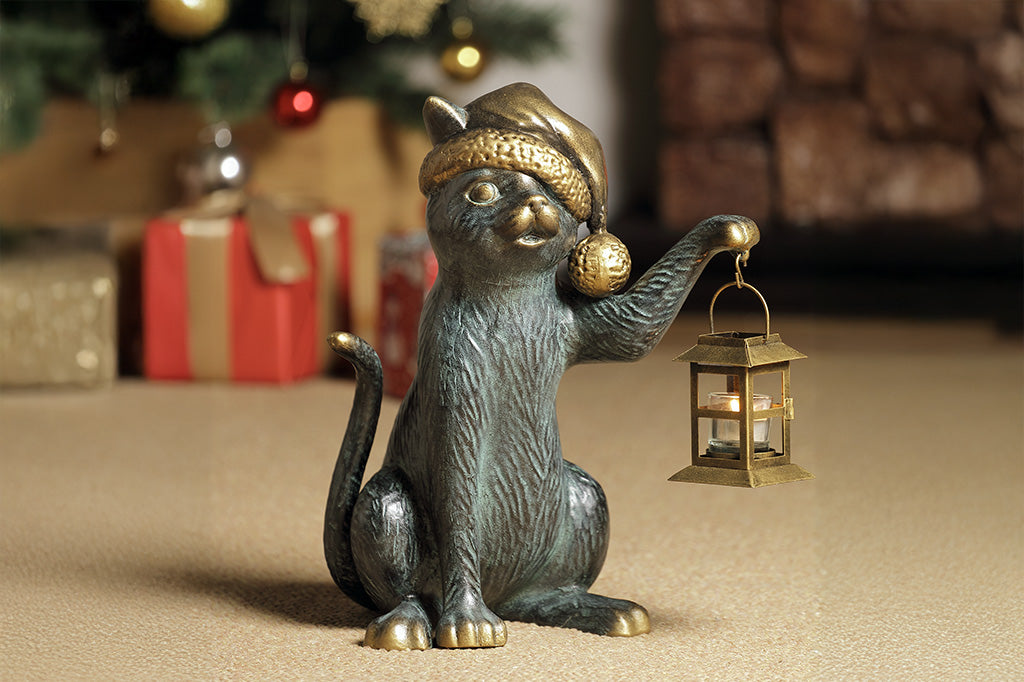Decorative cat figurine holding a lantern with Christmas decorations in the background