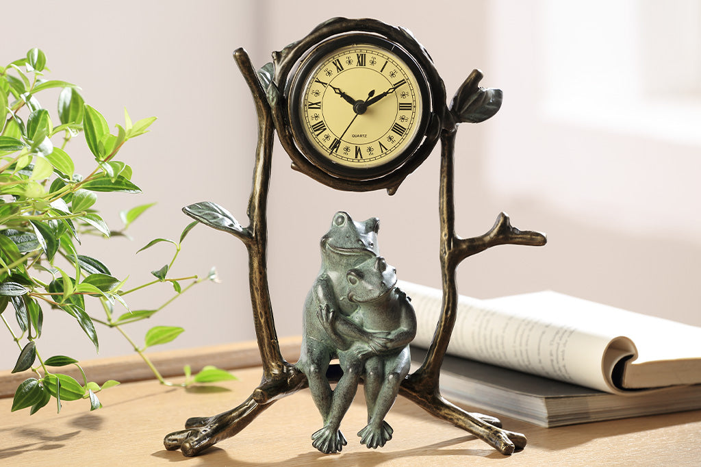 A clock with a sculpture of two frogs hugging while sitting on branches.