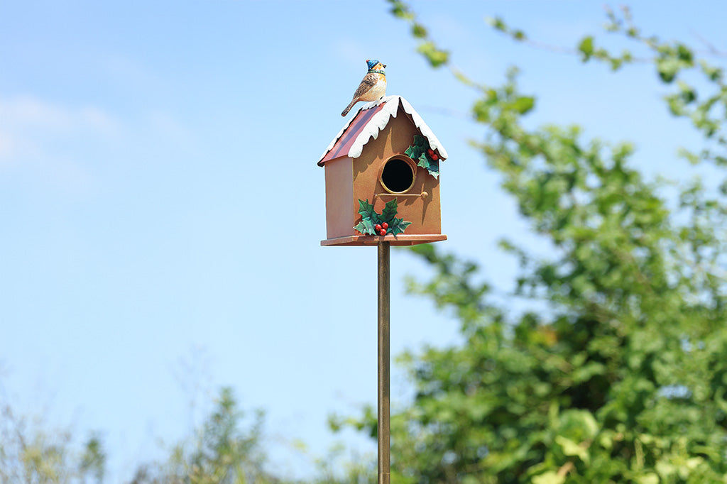 A holiday themed birdhouse with a bird wearing a knitted cap and scarf.
