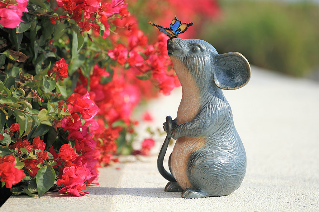 Statue of a mouse with a butterfly on its nose next to pink flowers