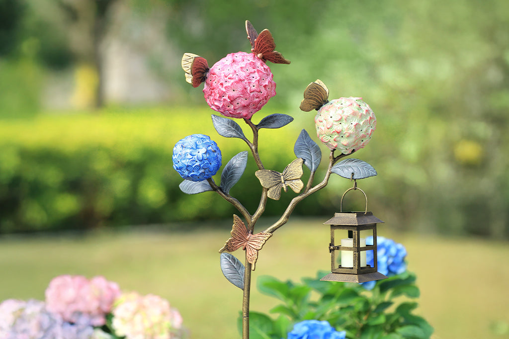 A garden stake lantern of 3 hydrangea flowers with a group of butterflies.