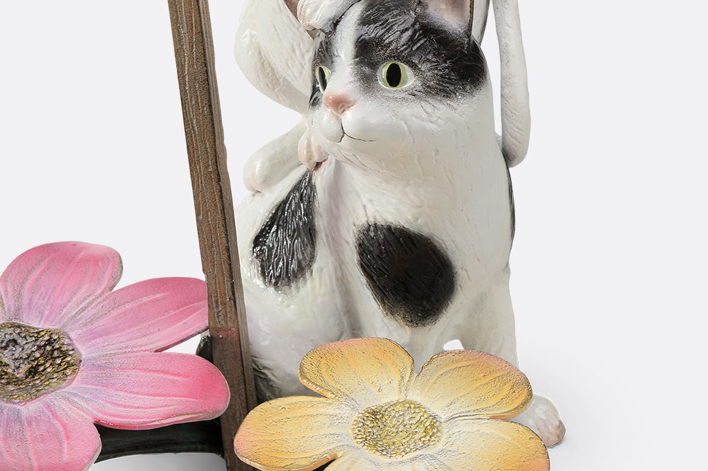 A garden sculpture of two cats holding a sign that says "love grows here" with a bird sitting on the sign and a pair of flowers at the bottom.