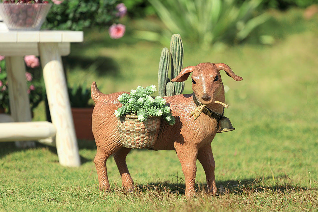 A planter sculpture of a goat with a bell carrying two baskets at his side.