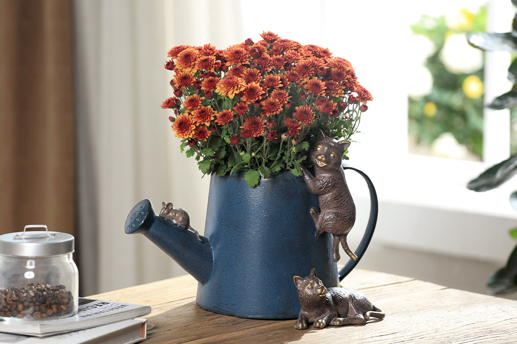 A decorative watering can planter with two cats climbing around to follow a mouse.