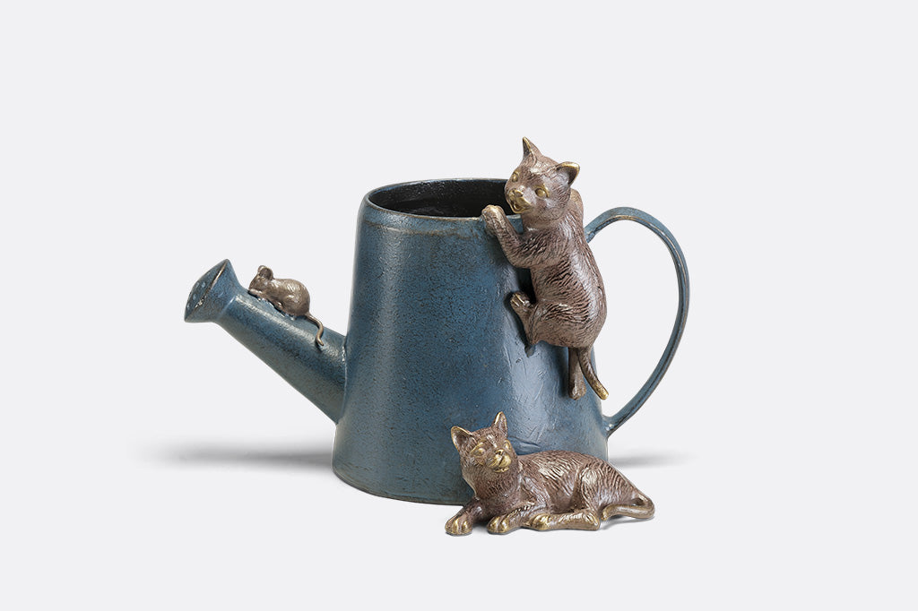 A decorative watering can planter with two cats climbing around to follow a mouse.