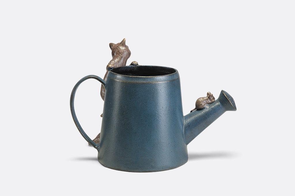 A decorative watering can planter with two cats climbing around to follow a mouse.