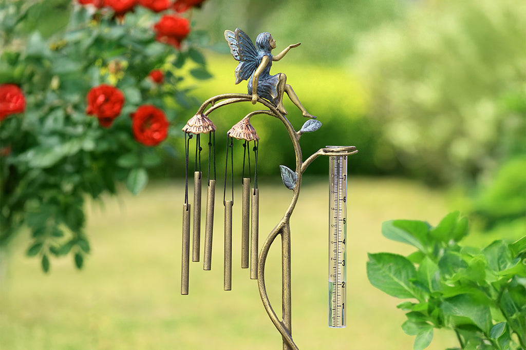 A staked raincatcher and windchime of a fairy sitting on flowers.