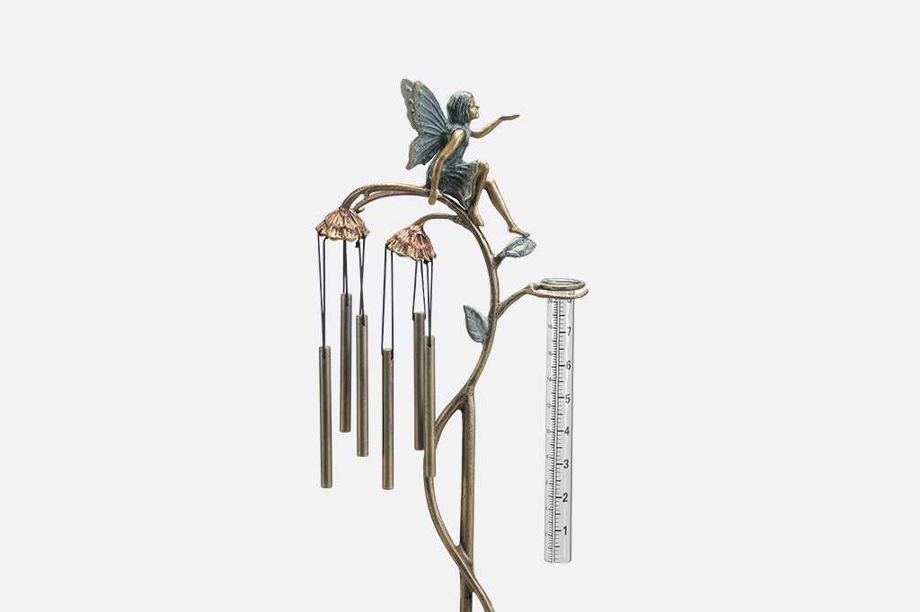 A staked raincatcher and windchime of a fairy sitting on flowers.