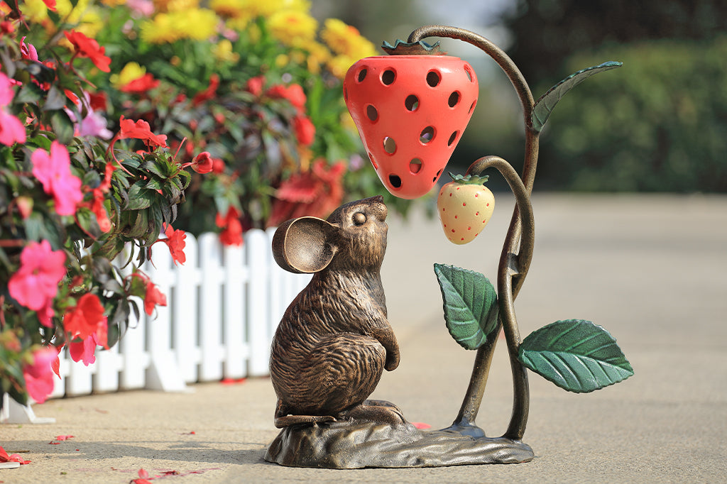 A sculpture of a mouse looking up at a strawberry shaped lantern.