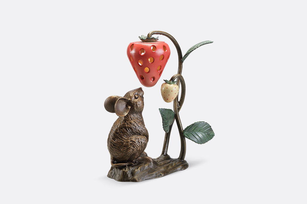 A sculpture of a mouse looking up at a strawberry shaped lantern.