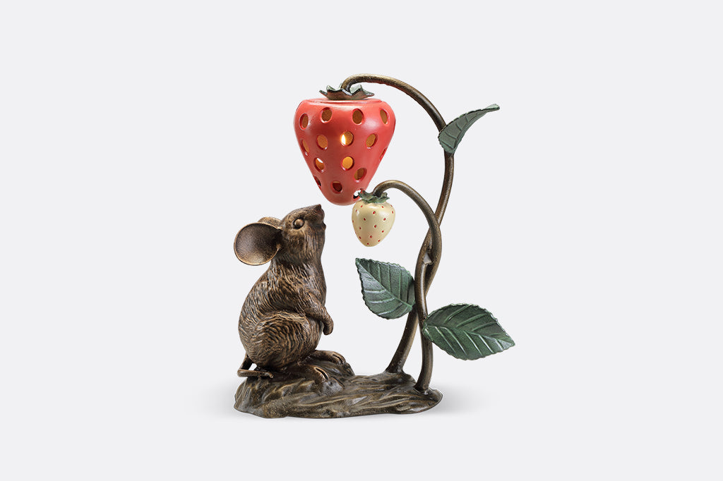 A sculpture of a mouse looking up at a strawberry shaped lantern.