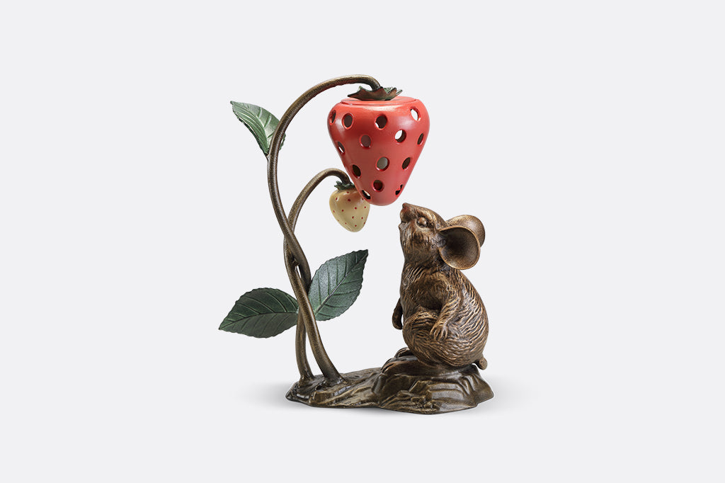 A sculpture of a mouse looking up at a strawberry shaped lantern.