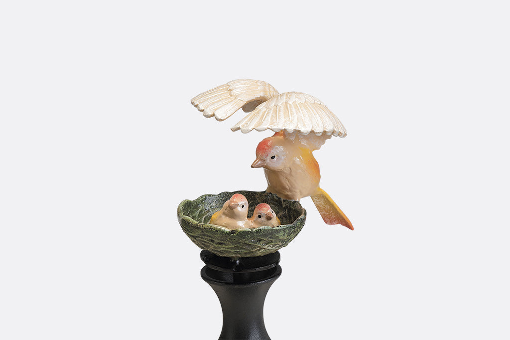 A hose guard sculpture of a mother bird sheltering her babies in their nest.