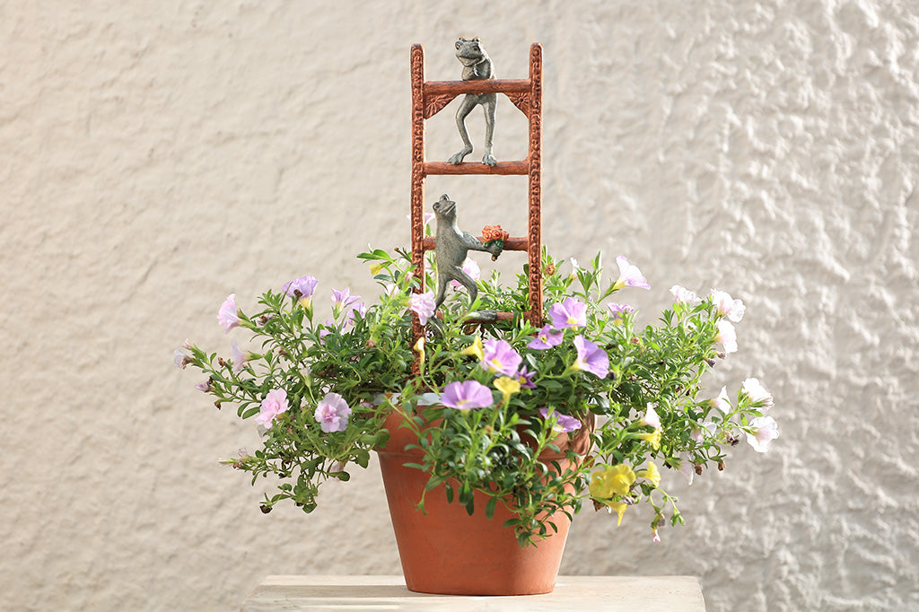 A Trellis of a Frog holding a flower coming up to meet another frog in a flower pot.