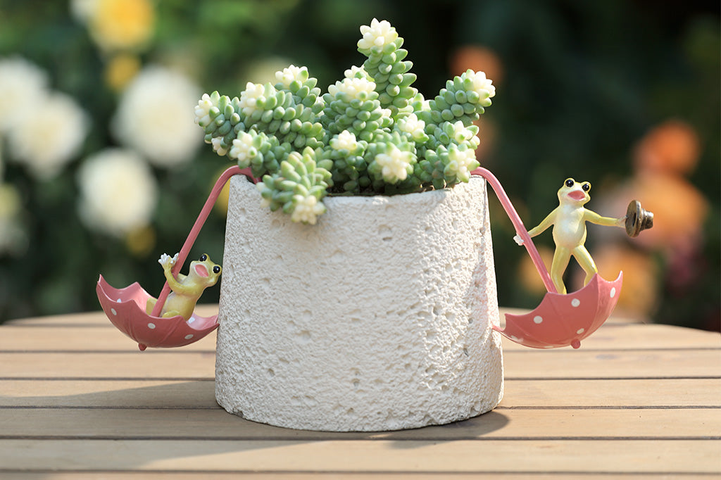 Pot hanging sculptures of dancing frogs inside of pink polka dot umbrellas.