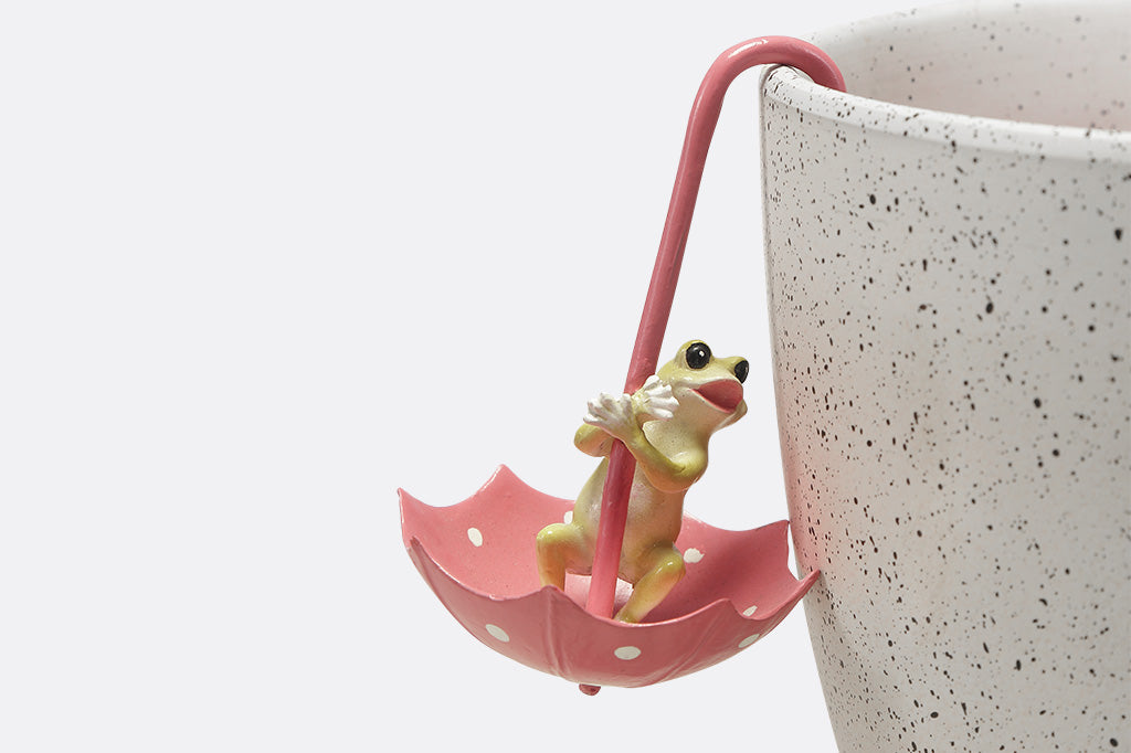 Pot hanging sculptures of dancing frogs inside of pink polka dot umbrellas.