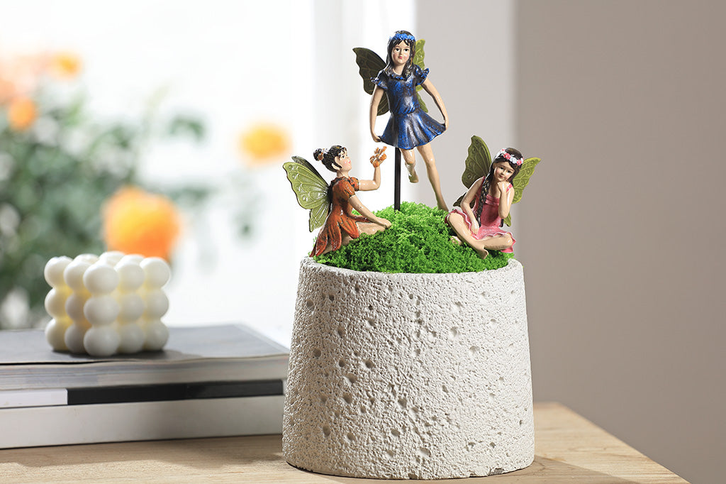 A trio of fairy sculpture plant pot stakes, one wearing pink, one wearing blue, and one wearing orange.