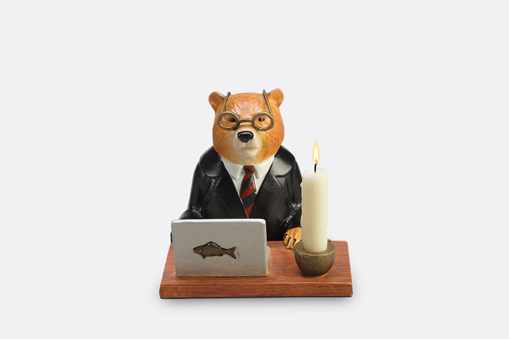 A sculpture of a bear wearing a suit on his Fishbook Pro laptop with a mug and candle.