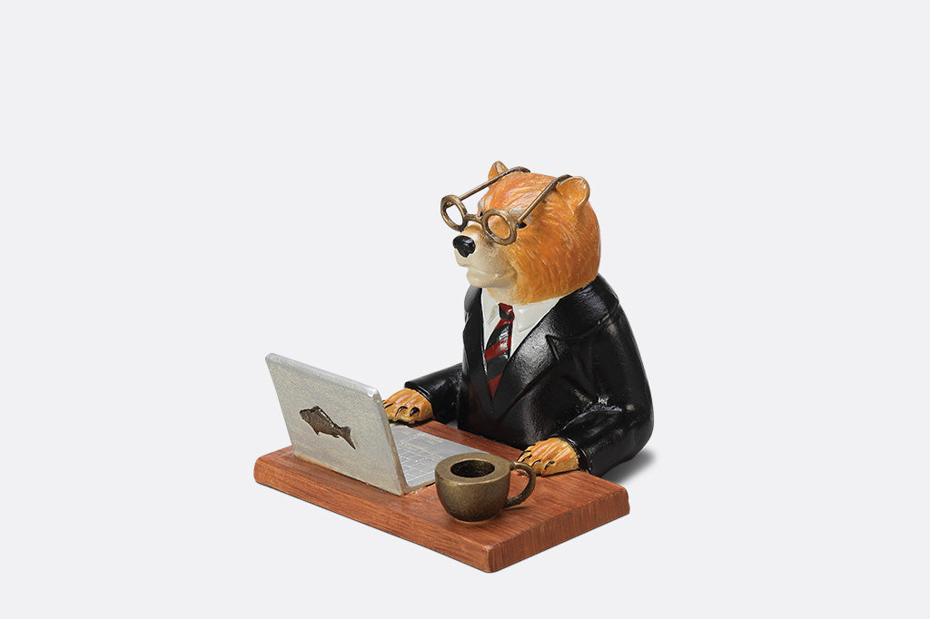 A sculpture of a bear wearing a suit on his Fishbook Pro laptop with a mug.