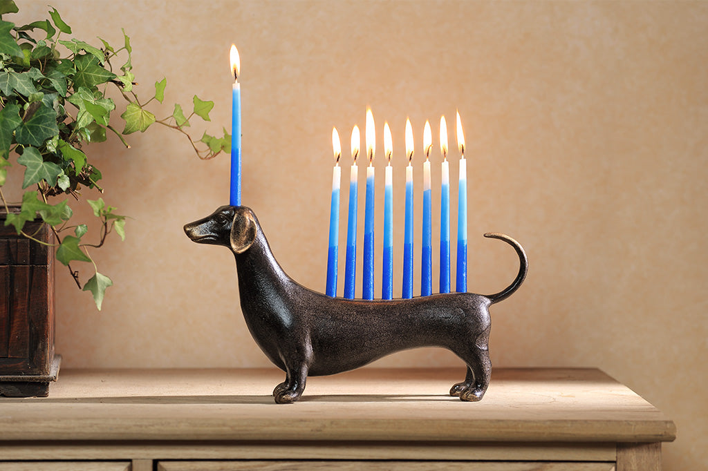 A dachshund-shaped Hanukkah menorah holding nine blue lit candles.