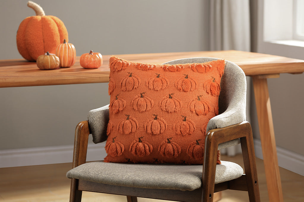 Chair with an orange pillow featuring pumpkin pattern in a room with pumpkins on a table.