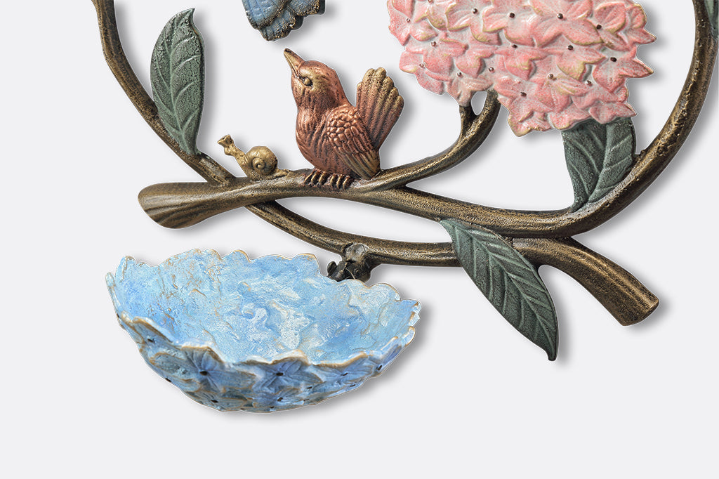 A round, wall mounted bird feeder with details of hydrangeas, leaves, birds, butterflies, and snails.