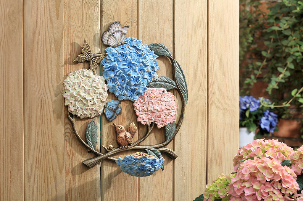 A round, wall mounted bird feeder with details of hydrangeas, leaves, birds, butterflies, and snails.