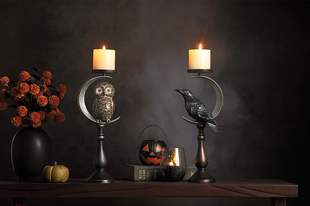 Halloween-themed candle holders with candles, pumpkins, and flowers on a dark background.