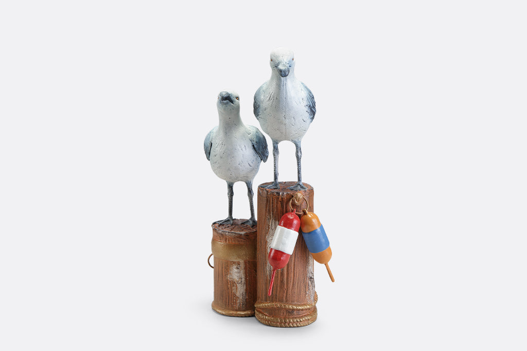 A sculpture of two seagulls standing atop the supporting beams of a dock adorned in buoys and rope.