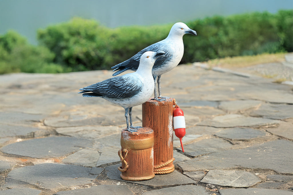 A sculpture of two seagulls standing atop the supporting beams of a dock adorned in buoys and rope.