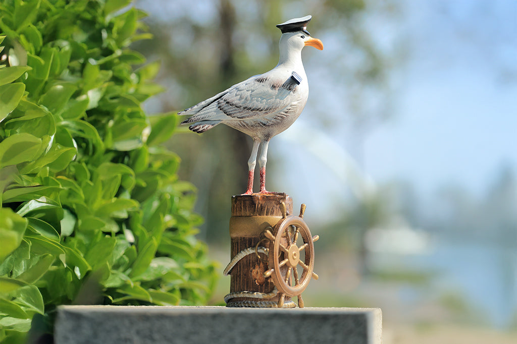 A sculpture of a seagull dressed in Captain regalia standing atop a dock adorned with rope and a ship's steering wheel.