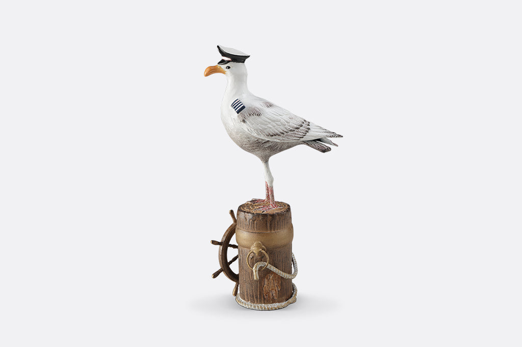 A sculpture of a seagull dressed in Captain regalia standing atop a dock adorned with rope and a ship's steering wheel.